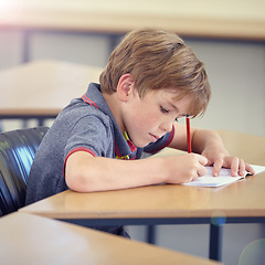 Image showing Child, student and writing in classroom for learning, education and development in language quiz or test. Smart boy or kid with notebook for school progress, creativity and knowledge at his desk