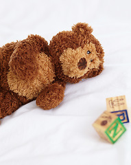 Image showing Teddy bear, toys and closeup in bedroom with building blocks on a mattress for still life of development. Learning, letters and objects for childcare and play in home with soft animal and alphabet