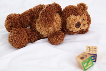 Image showing Teddy bear, closeup and toys in bedroom with building blocks on a mattress for still life of development. Learning, letters and objects for childcare and play in home with plush animal and alphabet
