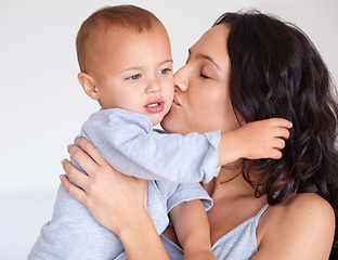 Image showing Family, kiss and mother with baby on a white background for bonding, relationship and relax in studio. Love, youth and happy mom embrace, hug and carry kid for growth, playing and child development