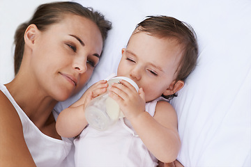 Image showing Baby, mother and drinking bottle for nutrition, liquid food and relaxing together on bed at home. Mommy, toddler and formula for health or child development in bedroom, feeding and milk for wellness