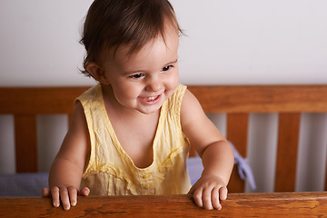 Image showing Baby in crib, playing with smile and fun in home, child development and care in home. Excited toddler girl in cot with playful face, energy and happiness in cute kids bedroom, nursery or apartment