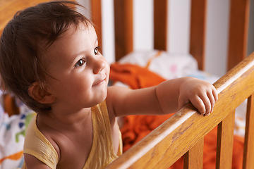 Image showing Baby girl in crib, playing with smile and fun in home, child development and care in home. Toddler in cot with playful face, energy and happiness in cute kids bedroom, nursery or apartment at bedtime