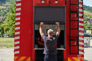 Image showing A dedicated firefighter preparing a modern firetruck for deployment to hazardous fire-stricken areas, demonstrating readiness and commitment to emergency response