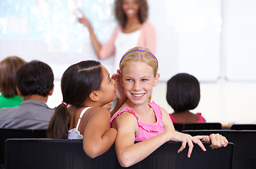 Image showing Kids, classroom and whisper in ear for secret, gossip or communication in lesson at school. Little girl, students or friends listening to rumor, information or surprise in class together with teacher