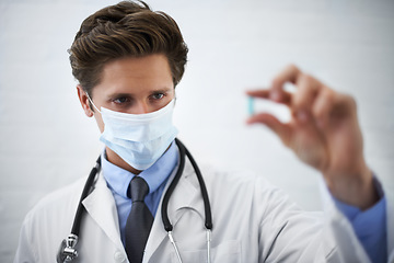 Image showing Man, doctor and checking pill with face mask for healthcare, cure or drugs on a white studio background. Male person, surgeon or medical nurse looking at medication in research, study or examination