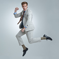 Image showing Businessman, celebration and jumping for success in portrait, studio and fist pump for triumph. Male person, professional and victory or accomplishment, cheering and energy or win by gray background