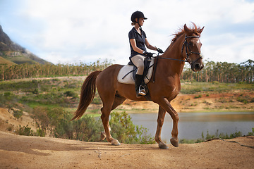 Image showing Equestrian, woman and riding a horse in nature on adventure and journey in countryside. Ranch, animal and rider outdoor with hobby, sport or walking a pet on farm with girl in summer at river