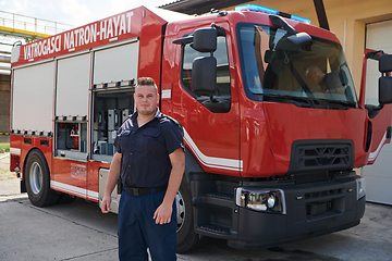 Image showing A confident firefighter strikes a pose in front of a modern firetruck, exuding pride, strength, and preparedness for emergency response