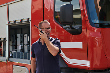 Image showing A dedicated firefighter, captured in a moment of communication, stands before a modern firetruck, showcasing the seamless integration of technology in emergency response