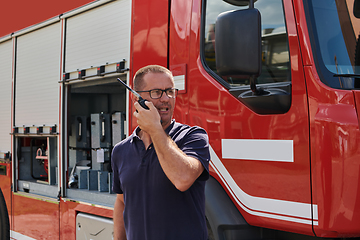 Image showing A dedicated firefighter, captured in a moment of communication, stands before a modern firetruck, showcasing the seamless integration of technology in emergency response