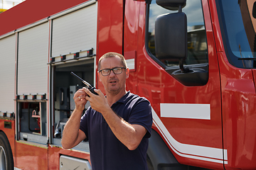 Image showing A dedicated firefighter, captured in a moment of communication, stands before a modern firetruck, showcasing the seamless integration of technology in emergency response