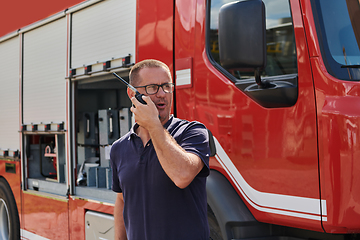 Image showing A dedicated firefighter, captured in a moment of communication, stands before a modern firetruck, showcasing the seamless integration of technology in emergency response