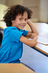 Image showing Portrait, student and boy in a classroom, education and relax with a book, learning and creative. Face, studying or kid with joy, child development or desk with notes, teaching or knowledge in school