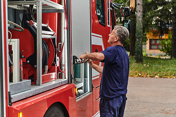 Image showing A dedicated firefighter preparing a modern firetruck for deployment to hazardous fire-stricken areas, demonstrating readiness and commitment to emergency response