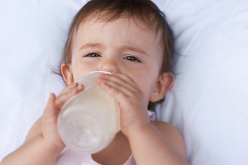 Image showing Baby, portrait and drinking milk for nutrition, liquid food and relax on bed at home. Girl, toddler and formula for health or child development in bedroom, feeding and bottle for wellness and growth