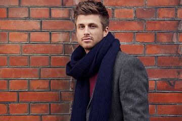 Image showing Portrait, fashion and winter with man on a brick wall background in the city for masculine style. Model, scarf and trendy outfit with a confident young person in an urban town for season clothing