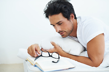 Image showing Relax, bedroom and man reading a book with glasses for knowledge on a weekend morning in his home. Education, study or learning with a casual young person lying on a bed for a hobby in his apartment