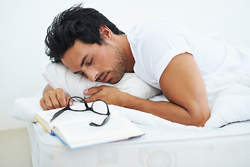 Image showing Sleeping, reading and a young man in the bedroom of his home with a book to relax or rest on the weekend. Study, learning or education with a tired person asleep on a book while lying in bed