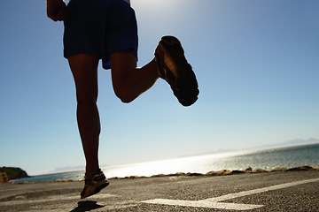 Image showing Person, running and asphalt at beach for fitness, workout or outdoor cardio training on a sunny day. Closeup of athlete legs on run, sprint or race on road or street by the ocean coast on mockup