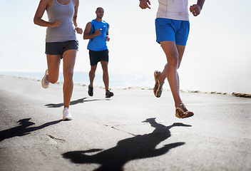 Image showing People, legs and running at beach for exercise, fitness or outdoor workout together on asphalt or road. Closeup of athletic group or runners in sports, teamwork or cardio training by the ocean coast