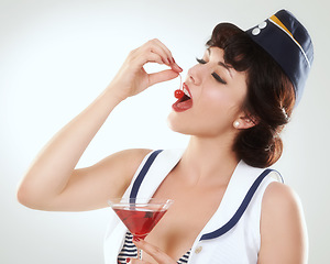 Image showing Cocktail, stewardess and woman eating cherry in studio isolated on white background. Red martini, glass and air hostess enjoy alcohol fruit, vintage pin up girl or flight attendant travel on journey