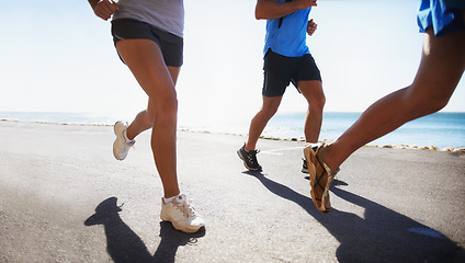 Image showing People, fitness and legs running at beach for exercise or outdoor workout together on asphalt or road. Closeup of athletic group or runners in sports, teamwork or cardio training by the ocean coast