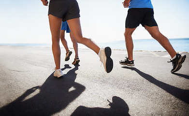 Image showing People, legs and running at beach for cardio, fitness or outdoor workout together on asphalt or road. Closeup of athletic group or runners in sports, teamwork or training exercise by the ocean coast