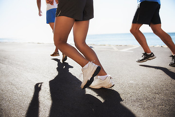 Image showing People, team and legs running at beach for cardio, fitness or outdoor workout together on asphalt or road. Closeup of athletic group or runners in sports or training exercise by the ocean coast