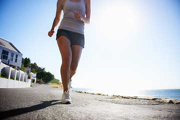 Image showing Woman, running and asphalt at beach for fitness, workout or outdoor cardio training on a sunny day. Closeup of athlete legs on run, sprint or race on road or street by the ocean coast on mockup space