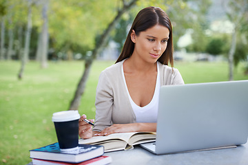 Image showing Student, books and coffee with laptop in park, technology and education by table for studying. College, young woman and commitment with outdoor by tea, focus and writing notes with online connection