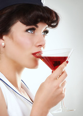 Image showing Glass, flight attendant and woman drink alcohol in studio isolated on a white background. Martini, red cocktail and an air hostess enjoy beverage, vintage pin up girl or stewardess travel on journey