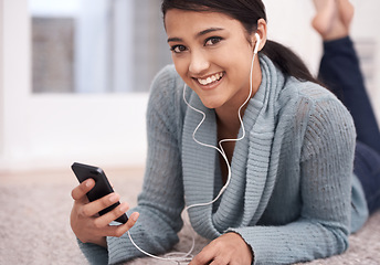 Image showing Portrait of happy woman on carpet with phone, headphones and relax with mobile app for podcast in house. Face of girl lying on floor with smile, music and streaming service for online radio in home.