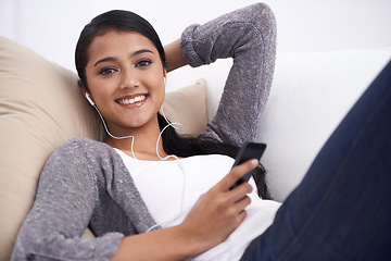 Image showing Young woman, phone and earphones, relax on couch with social media, communication and music in portrait. Listen to radio, podcast or watch video online, web or blog with mobile app and tech at home