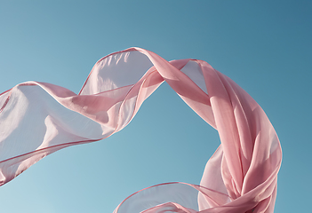 Image showing Flying pink fabric wave on blue sky background and illuminated b