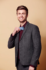 Image showing Portrait, fashion and smile with a young man in studio on a tan background to wear a trendy bowtie. Happy, style and clothes with a confident model in a retro or vintage suit for a formal event