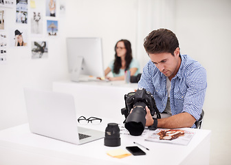 Image showing Camera, office and photographer looking at photoshoot in a studio or workshop for production. Creative, photography and young artist with dslr equipment for picture inspection in modern workplace.