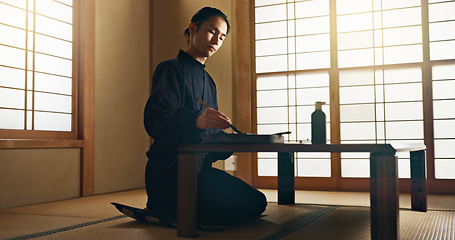 Image showing Man, calligraphy or creative Japanese artist in studio for art and script, letter with table, paper or alphabet. Asian, brush or person with tools, paintbrush and focus with traditional stationery