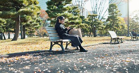 Image showing Japanese woman, bench and smartphone in park with relax, happiness and social media in sunshine in city. Female person, sitting and wellness with cellphone in town, streaming and digital technology