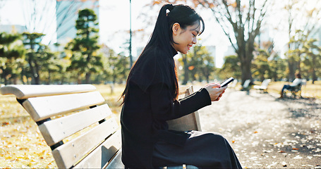 Image showing Happy asian woman, phone and typing on park bench for social media, communication or networking. Female person smile in relax on mobile smartphone for online search, streaming or reading in nature