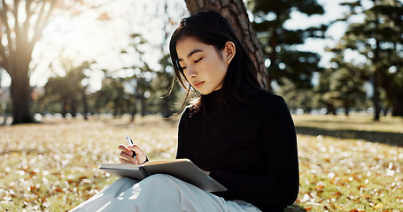 Image showing Japanese woman, writing and book in park, thinking and relax by tree, grass or sunshine for peace. Girl, person or student with story in nature, college or notes with vision, knowledge or campus lawn