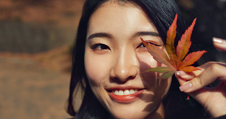 Image showing Woman, Asian and face with leaf in autumn, nature and color with happiness outdoor. Environment, plant and smile in portrait, park or garden in Japan with foliage, mockup space and positivity