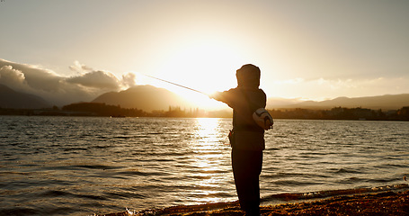 Image showing Person, fishing and water in morning, sunrise and sport by ocean, lake and river with equipment in nature. Fisherman, line and catch fish for games, food and silhouette in sunshine, dawn and horizon