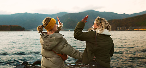 Image showing Women friends, hug and back at beach with care, love and outdoor with high five, support or celebration on travel. Girl, cheers and achievement with boat, water or lake with bonding by river in Japan