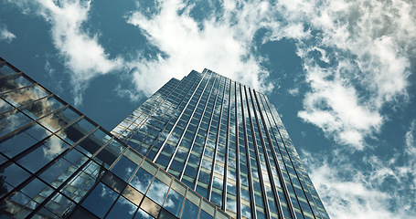 Image showing Low angle, skyscraper building and clouds with reflection, nature or urban infrastructure in city. Architecture, cityscape and skyline and metro with landscape, glass and sky background in timelapse