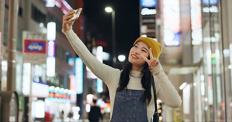 Image showing Peace, hands and selfie by Japanese woman in a city for travel, adventure or journey outdoor. V sign, emoji or happy lady influencer in Japan for content creation, blog or social media live streaming