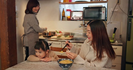 Image showing Family, Japanese and mother feeding kid in kitchen of home for growth, health or nutrition. Food, daughter eating in Tokyo apartment with parent and grandparent for diet or child development