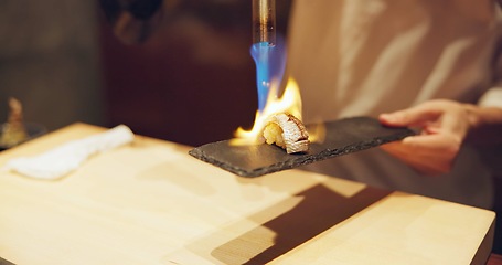 Image showing Hands, fire and cooking sushi with chef in restaurant for traditional Japanese food or cuisine closeup. Kitchen, flame for seafood preparation and person working with gourmet meal recipe ingredients