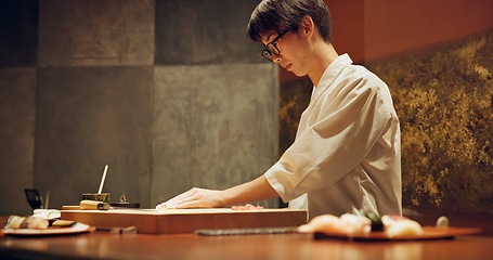 Image showing Chef, restaurant or japanese sushi as fish, raw salmon or healthy food for local culture in kitchen. Asian man, hands and skill in rice on wood board, table and catering of seafood menu for nutrition