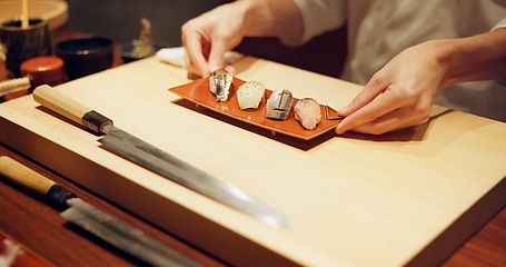 Image showing Hands, food and chef serving sushi in restaurant for traditional Japanese cuisine or dish closeup. Kitchen, cooking or seafood preparation and person working on table with gourmet meal ingredients